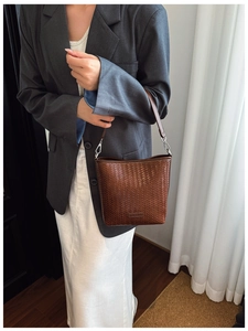 Détail d'un sac seau tressé marron foncé porté avec un blazer gris et une jupe blanche