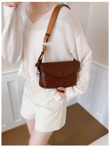 Sac bandoulière tissé marron avec large sangle porté dans un décor minimaliste