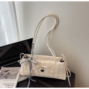 Detail of cream checkerboard shoulder bag featuring a leather bow and metal heart charm
