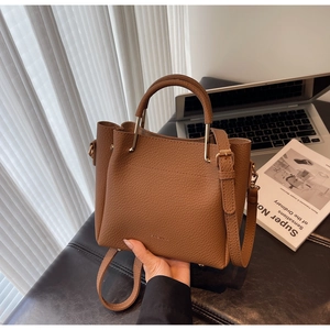 Detailed close-up of brown pebbled leather bucket bag with metallic round handles