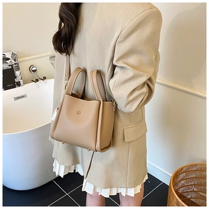 Detail view of the beige lychee pattern leather bucket bag carried by a model