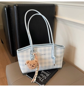 Detail of light blue gingham tote bag with teddy bear charm and striped ribbon accent