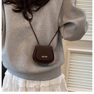 Detailed view of mini brown leather saddle bag with gold orin lettering on flap