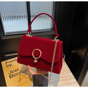 Close-up of red velvet handbag featuring a golden ring clasp and decorative knot handle