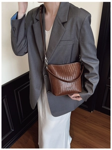 Détail du sac seau tressé marron foncé porté avec un blazer gris au style moderne