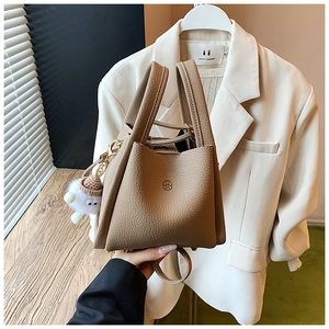 Detail of a brown lychee pattern leather bucket bag with top handles and plush charm