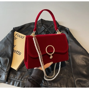 Detail of red velvet handbag with golden ring lock and pearl chain on vintage books