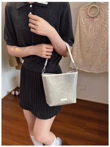 Détail du sac seau tressé argenté avec logo en métal et bandoulière en cuir blanc
