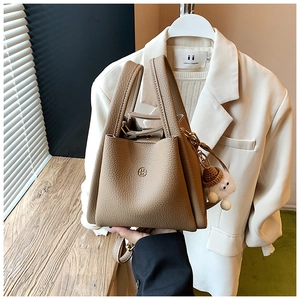Detail of khaki lychee grain leather bucket bag with UM logo and plush doll pendant