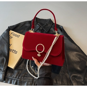 Detail of red velvet bag featuring golden ring, shell pendant and pearl chain strap