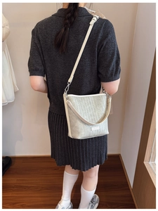 Détail d'un sac seau beige à texture tissée avec logo métallique et bandoulière