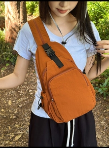 Detailed view of an orange nylon sling bag with multi-zipper pockets on a model outdoor