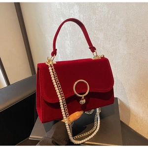 Close-up of luxury red velvet handbag featuring gold heart clasp and pearl chain strap