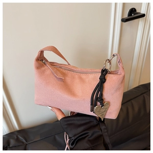 Detail of pink suede shoulder bag featuring a black braided rope and gold heart pendant