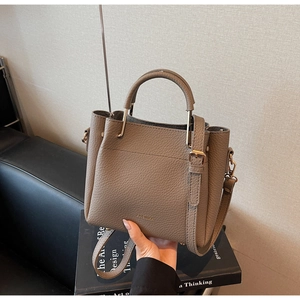 Detail of taupe pebbled leather handbag with arched handle and brand logo