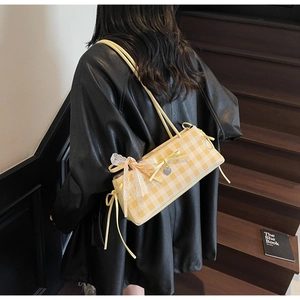 Detail of yellow plaid shoulder bag with lace bow and heart charm worn by model