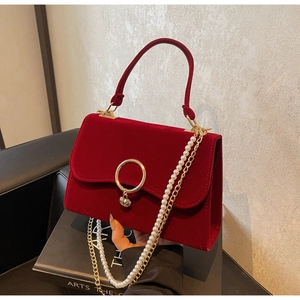 Detail of red velvet handbag with golden ring closure and elegant pearl chain strap