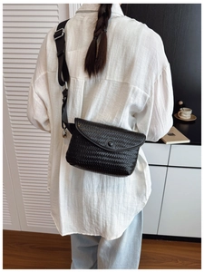 Détail d'un sac bandoulière noir tressé avec bandoulière large sur un mannequin