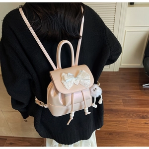 Detail of a mini beige backpack with lace bow, heart charm and white plush pendant