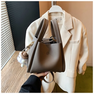 Detail of grey lychee leather bucket bag with double handles and plush charm