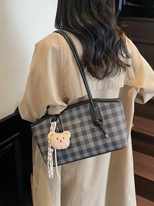 Checkerboard pattern tote bag with teddy bear charm shown as a shoulder bag on a model