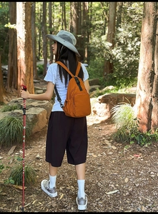 Orange waterproof nylon mini backpack worn by a hiker on a forest trail path