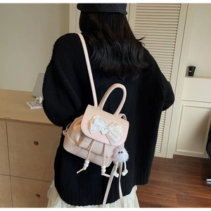 Detail of pink mini backpack with lace bow, heart charm and white plush monster keychain
