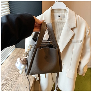 Close-up of brown pebbled leather bucket bag with brand logo and plush charm
