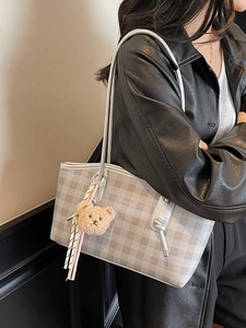 Women's grey checkerboard tote bag with bear charm and ribbon shown on shoulder