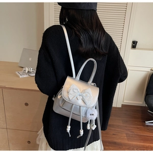 Silver mini backpack with white lace bow and plush charm on a model in a cozy room