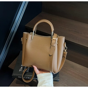 Close-up of brown litchi pattern leather bucket bag with gold hardware on wooden stairs