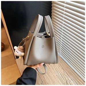 Detail of grey lychee leather bucket bag with top handles and plush lamb charm