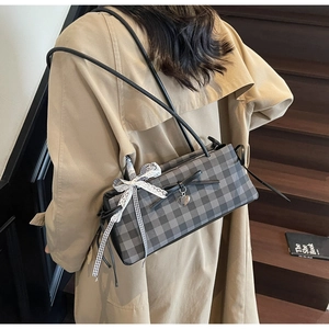 Detail of grey plaid shoulder bag with black bow and heart pendant on a trench coat