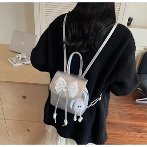 Silver mini backpack with white lace bow and plush charm shown on a female model