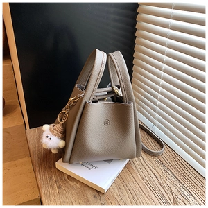 Detail view of taupe lychee leather bucket bag with gold hardware and plush charm