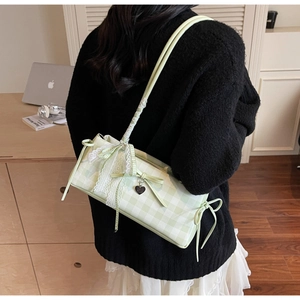 Detail of green checkerboard shoulder bag with lace edges and bow charms shown on a model