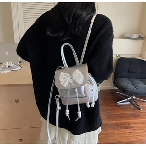 Detail of silver mirror backpack with white lace bow and heart charm on a black outfit