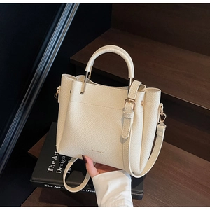 Close-up of beige lychee texture leather bucket bag with gold hardware and logo