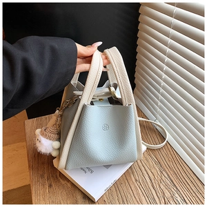 Detail of light blue bucket bag with cream litchi leather handle and a cute pom-pom charm