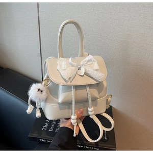 Detail of cream PU leather backpack featuring lace bow, heart pendant, and plush monster charm