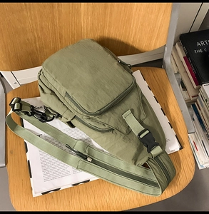 Detail of pea green nylon crossbody bag with multi-zipper pockets on a wooden chair