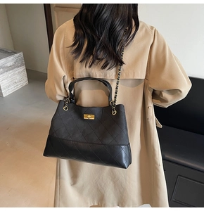 Detail of black quilted tote bag with gold clasp and chain strap on a trench coat