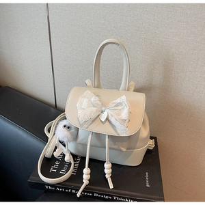 Detail of cream white mini backpack with lace bow and plush charm on art books