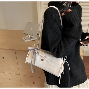 Close-up of beige plaid shoulder bag featuring lace bow details and a heart charm