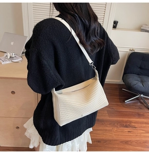 Dettaglio di una borsa a tracolla intrecciata color crema con trama fine e cinturino in pelle