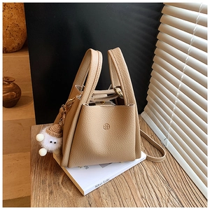 Beige lychee pattern bucket bag with UM logo and plush lamb pendant on wooden desk