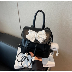 Detail of black faux leather mini backpack with white lace bow and plush charm