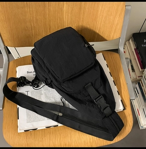 Detail of black pleated nylon crossbody bag with buckle and zipper on a wooden chair