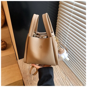 Close-up of beige lychee leather bucket bag with dual handles and plush ball charm