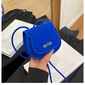 Close-up of a mini blue crossbody saddle bag with a yellow orin logo and slim shoulder strap